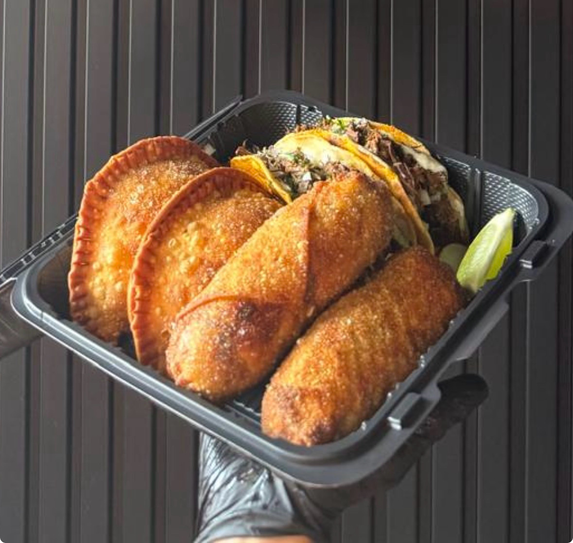 Birriaholic sampler with birria tacos, empanadas and eggrolls in a black takeout tray